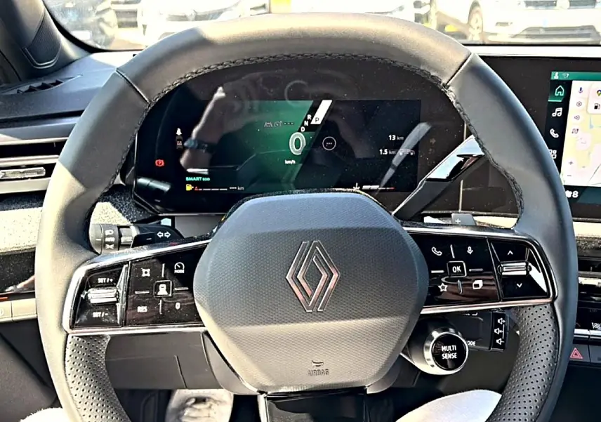 Vue rapprochée du volant noir multifonction de la Renault Clio VI avec tableau de bord numérique en arrière-plan.