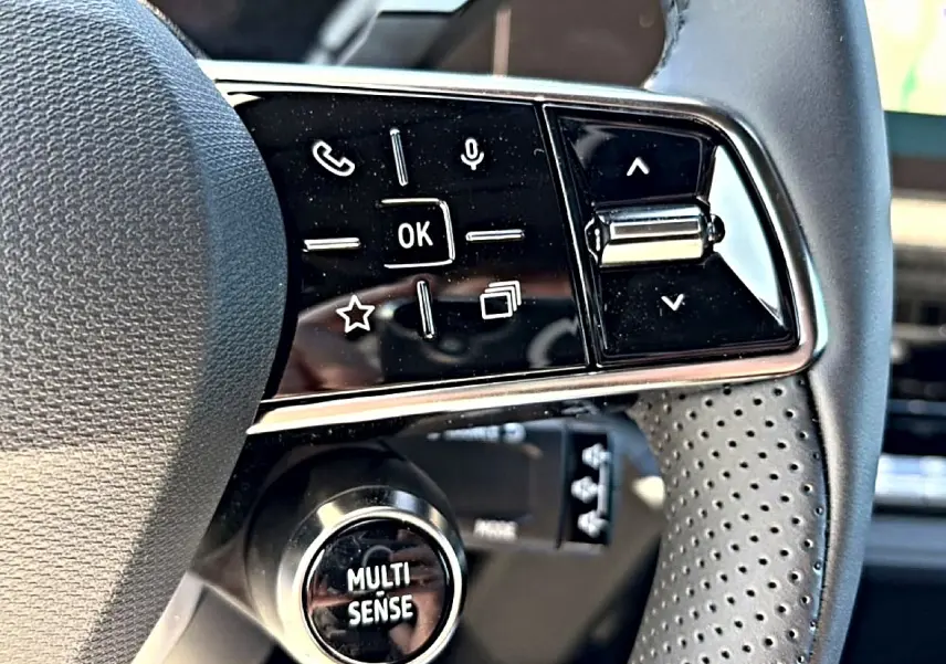 Gros plan sur les commandes multifonctions noires du volant perforé de la Renault Clio VI noire, bouton Multi-Sense visible.