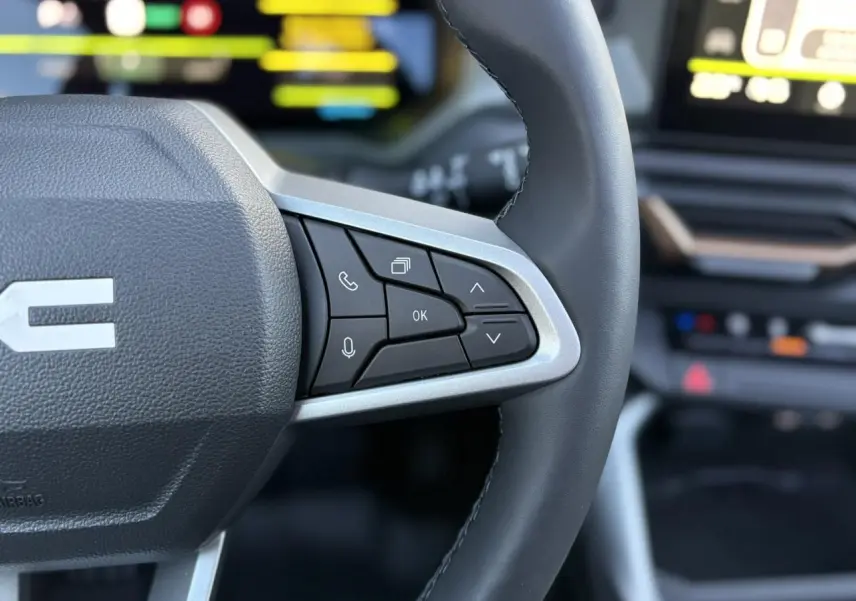 Gros plan sur le volant noir avec commandes multifonctions du DACIA BIGSTER 2025, intérieur moderne et écran flou en arrière-plan