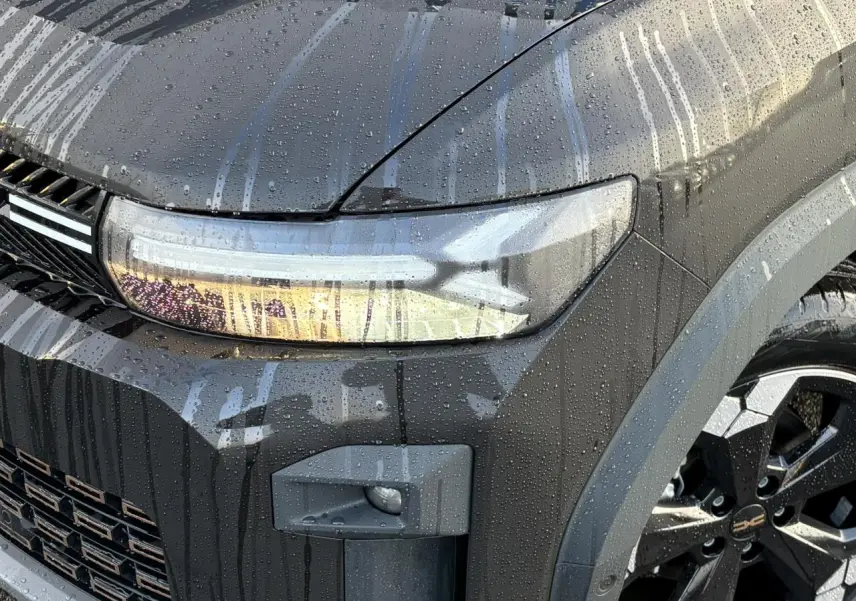 Gros plan sur l'avant droit noir nacré du Dacia Bigster 2025 avec phare allumé et jante alliage diamantée noire.