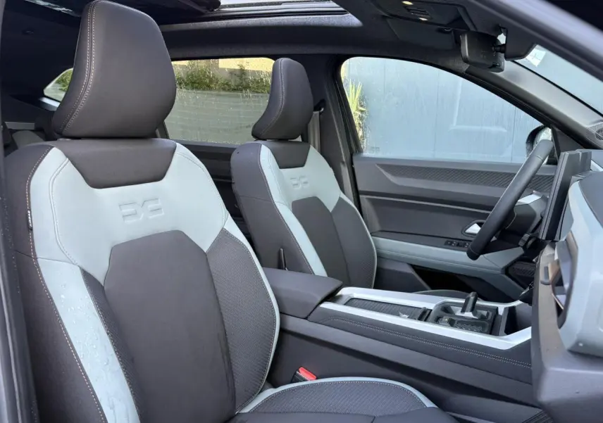 Vue intérieure côté conducteur du Dacia Bigster 2025, sièges Extreme TEP MicroCloud gris clair et foncé avec toit panoramique ouvert.