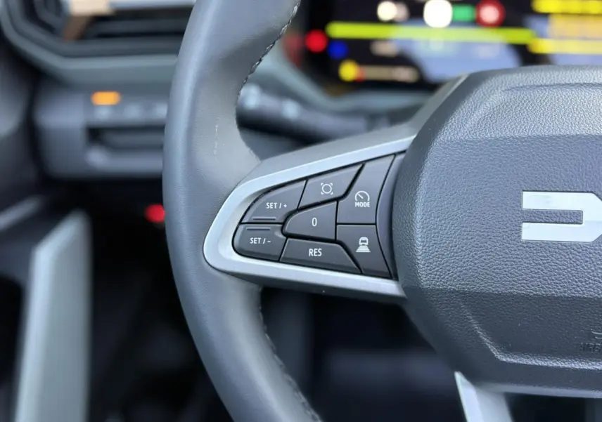 Gros plan sur le volant gris du Dacia Bigster 2025, avec commandes intégrées et logo central partiel visible.