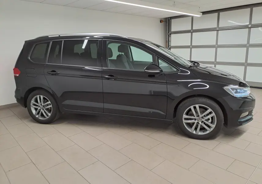 Vue de profil côté gauche d'un Volkswagen Touran 2025 noir intense nacré, avec jantes alliage et vitrage teinté.