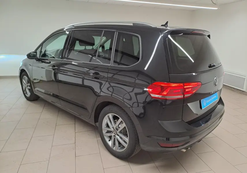 Vue 3/4 arrière droit du Volkswagen Touran noir intense nacré, avec feux arrière allumés et jantes alliage visibles.
