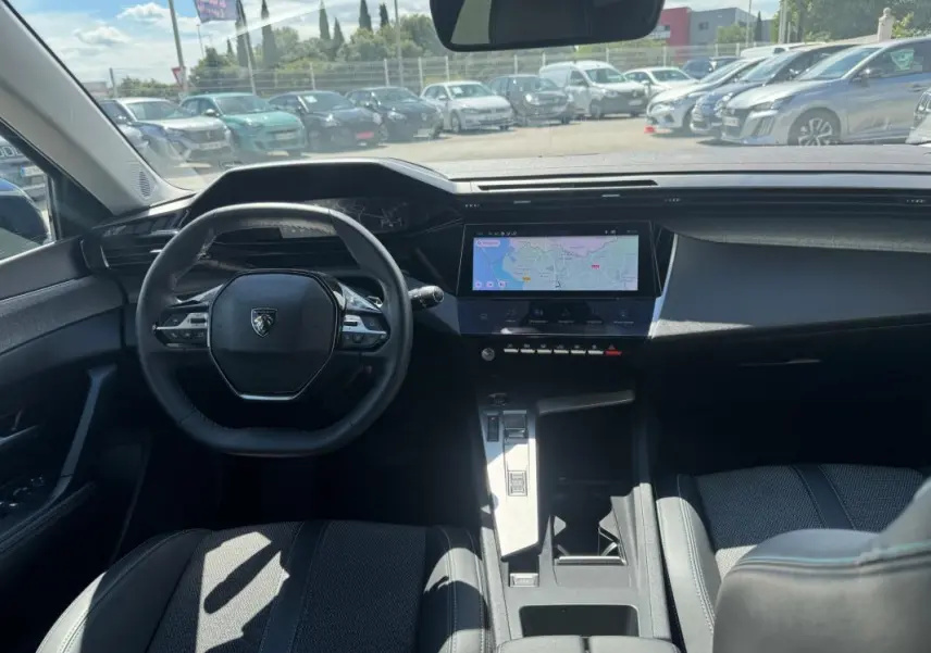 Vue intérieure avant de la Peugeot 308 Hybrid 136 e-DCS6 Allure 2024, tableau de bord avec écran tactile et volant compact noir.