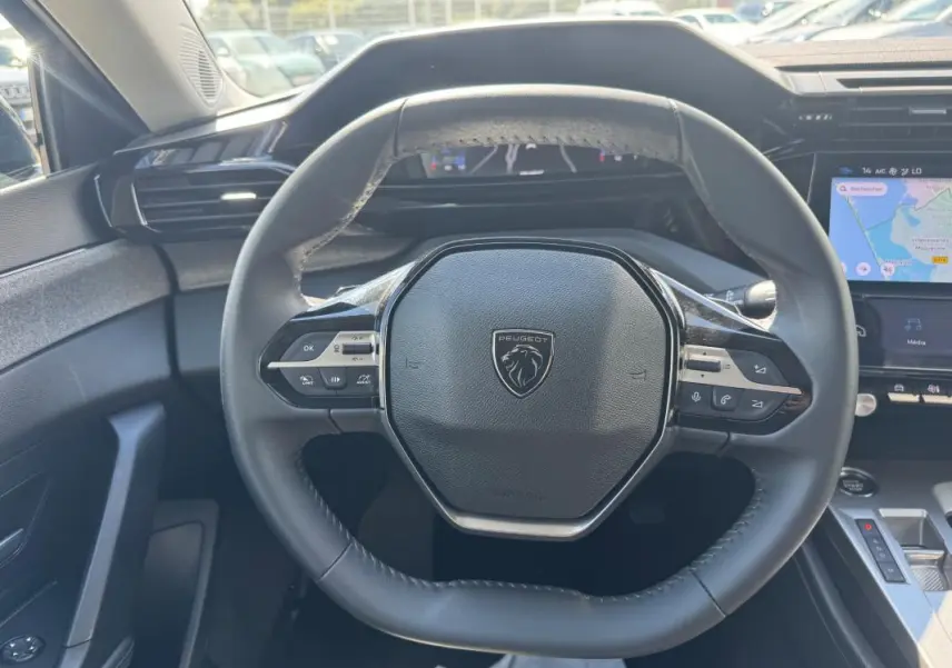 Vue intérieure centrée sur le volant noir de la Peugeot 308 Hybrid 2024 avec tableau de bord numérique et écran tactile.