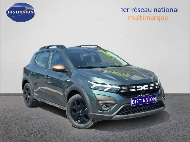 Vue 3/4 avant droite d'une Dacia Sandero Stepway 2025 vert cèdre métallisé avec jantes noires et barres de toit.