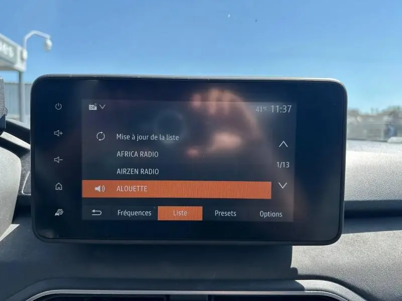 Écran tactile central du tableau de bord de la Dacia Sandero 2025 affichant la liste des radios en extérieur lumineux.