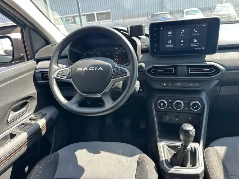 Vue intérieure avant du tableau de bord et volant noir de la Dacia Sandero 2025 avec écran tactile et levier de vitesses manuel.