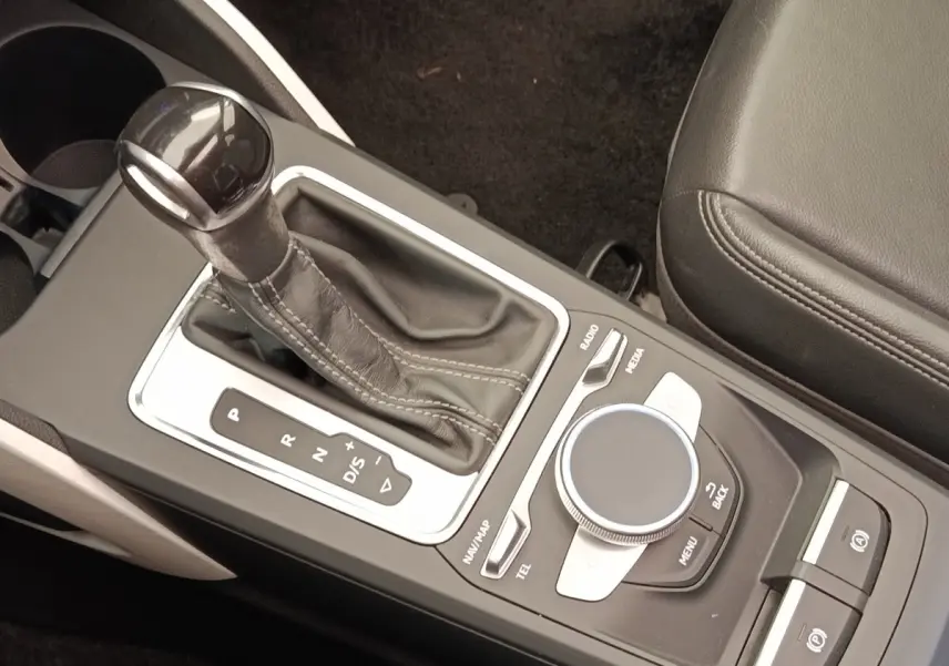 Gros plan sur la console centrale de l’Audi Q2 noire, avec levier de vitesse automatique et molette de commande multimédia.