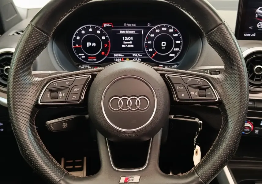 Vue rapprochée du volant cuir perforé Audi Q2 S Line 2021 avec tableau de bord numérique et commandes multifonctions.