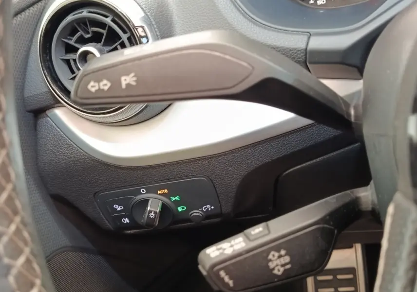 Détail intérieur côté gauche du tableau de bord noir d’un Audi Q2 35 TFSI 2021 avec commandes d’éclairage et aérateur rond.