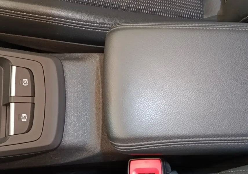 Gros plan sur la console centrale noire de l'Audi Q2 35 TFSI S Line 2021, avec accoudoir cuir et commandes frein électrique.
