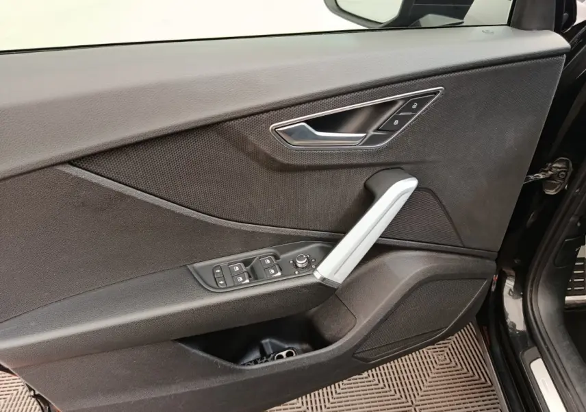 Vue rapprochée de la porte avant gauche noire d'un Audi Q2 35 TFSI S Line, avec commandes de vitres et poignée argentée.