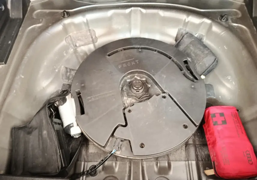 Vue plongeante sur le coffre d’un Audi Q2 noir 2021, montrant la roue de secours et une trousse de secours rouge.