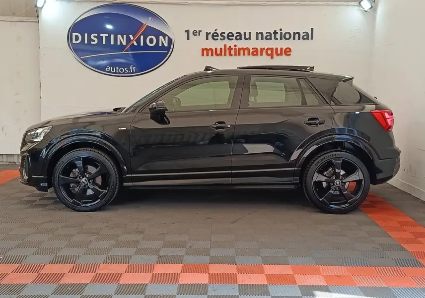 Profil côté gauche d’un Audi Q2 35 TFSI S Line noir 2021, avec jantes noires et toit ouvrant en intérieur showroom.