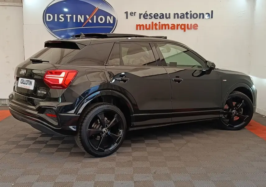 Audi Q2 35 TFSI S Line noir en vue profil côté droit, avec jantes noires et vitres teintées, en intérieur showroom.