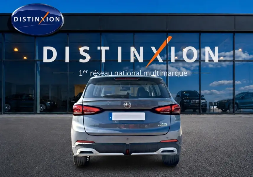 Vue arrière d'un MG Motor ZS gris 1.5 hybrid 197 luxury garé devant une vitrine Distinxion.