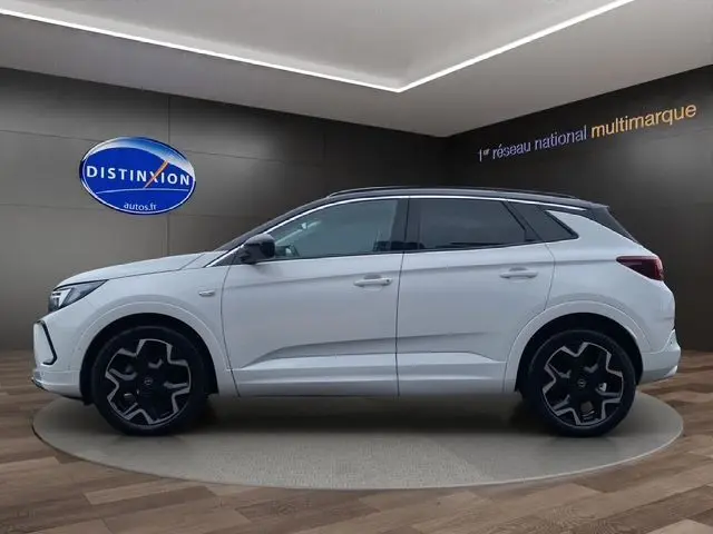 Profil côté gauche d'un Opel Grandland blanc Arktis avec toit noir, jantes 19 pouces et lignes épurées en showroom.