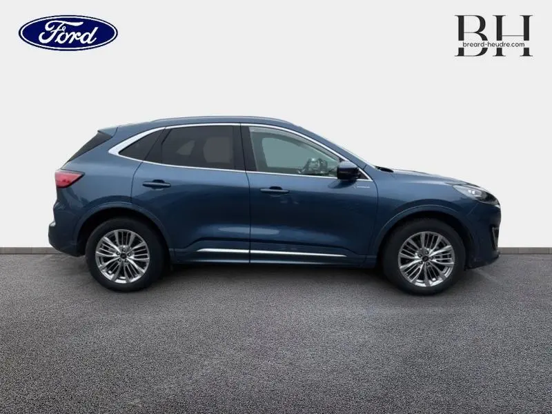 Profil droit d'un Ford Kuga 2022 bleu azur métallisé avec jantes alu et toit panoramique visible sur fond neutre.