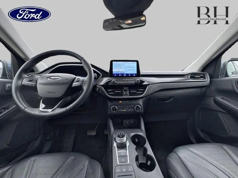 Vue intérieure avant du Ford Kuga 2022 avec tableau de bord noir, écran tactile central et volant cuir multifonction.