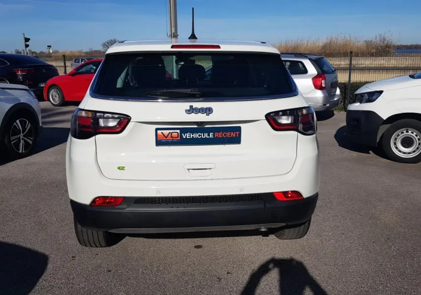 Vue arrière d'un Jeep Compass blanc 2024 avec feux LED et logo e-Hybrid sur un parking extérieur.