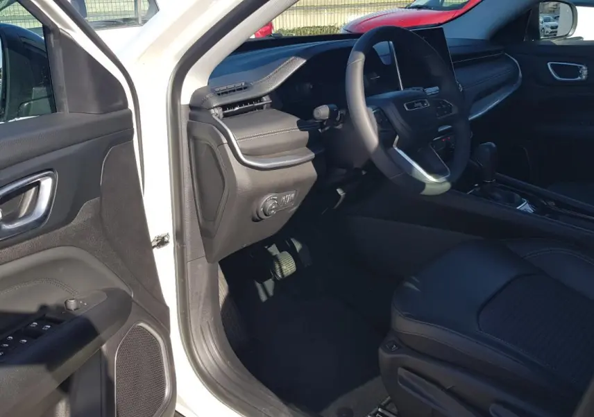 Vue intérieure côté conducteur du Jeep Compass blanc 2024, montrant le volant, tableau de bord et siège en cuir noir.