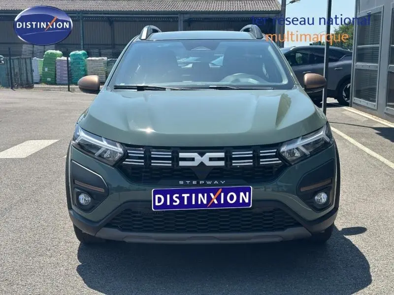 Vue avant d'une Dacia Sandero Stepway 2025 en Vert Cèdre métallisé avec calandre noire et barres de toit visibles.