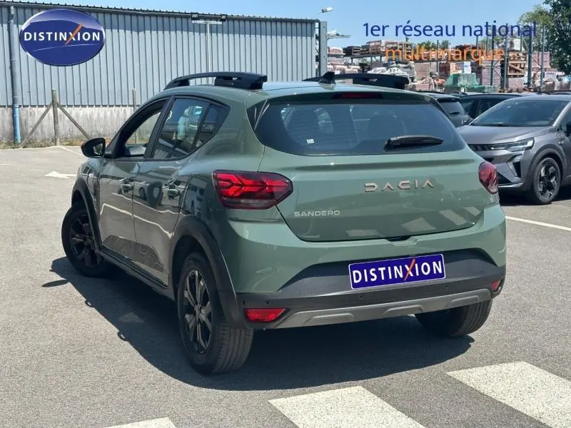 Vue 3/4 arrière droite d'une Dacia Sandero Stepway 2025 vert cèdre métallisé avec barres de toit et jantes alu noires.