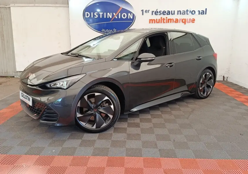 Vue 3/4 avant droite d'une CUPRA BORN gris foncé avec jantes noires et détails sportifs visibles en intérieur showroom.