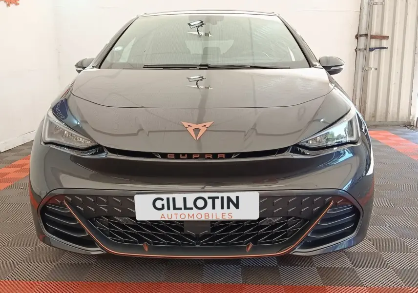 Vue avant d'une CUPRA Born gris foncé avec logo cuivre et calandre noire soulignée d'orange dans un showroom.