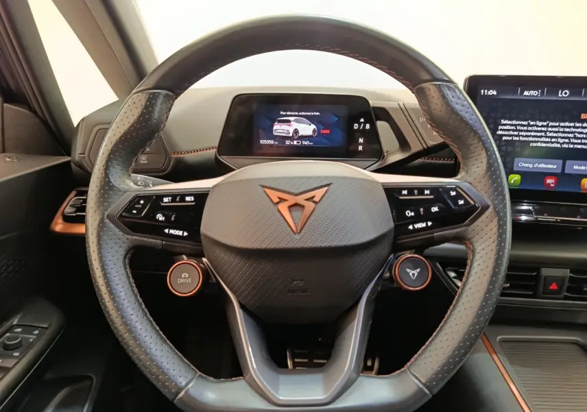 Vue rapprochée du volant cuir perforé gris foncé avec logo CUPRA orange et tableau de bord numérique du CUPRA BORN 2023.
