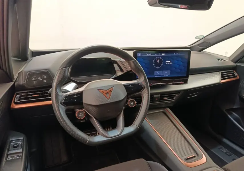 Vue intérieure avant du CUPRA BORN gris foncé, volant cuir avec logo, grand écran tactile central et détails cuivrés sur la planche de bord.