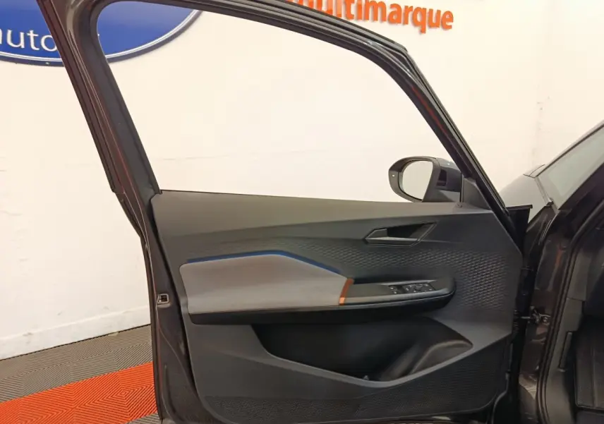 Vue intérieure de la porte avant gauche gris foncé du CUPRA BORN 230ch avec détails de commandes et habillage texturé.