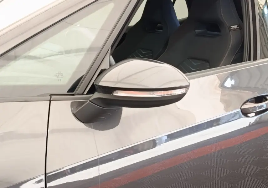 Gros plan sur le rétroviseur côté gauche gris foncé d’une CUPRA BORN 230ch avec siège sport visible à l’intérieur.