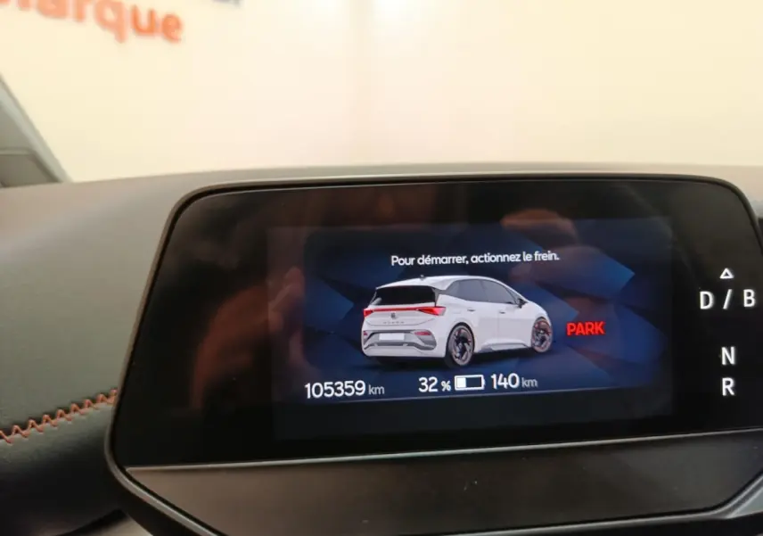 Écran numérique montrant une CUPRA Born blanche en vue arrière 3/4 avec indicateur de charge et kilométrage.