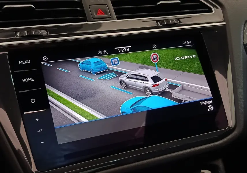 Écran tactile central montrant l'aide à la conduite avec représentation graphique d'un Volkswagen Tiguan blanc en circulation.
