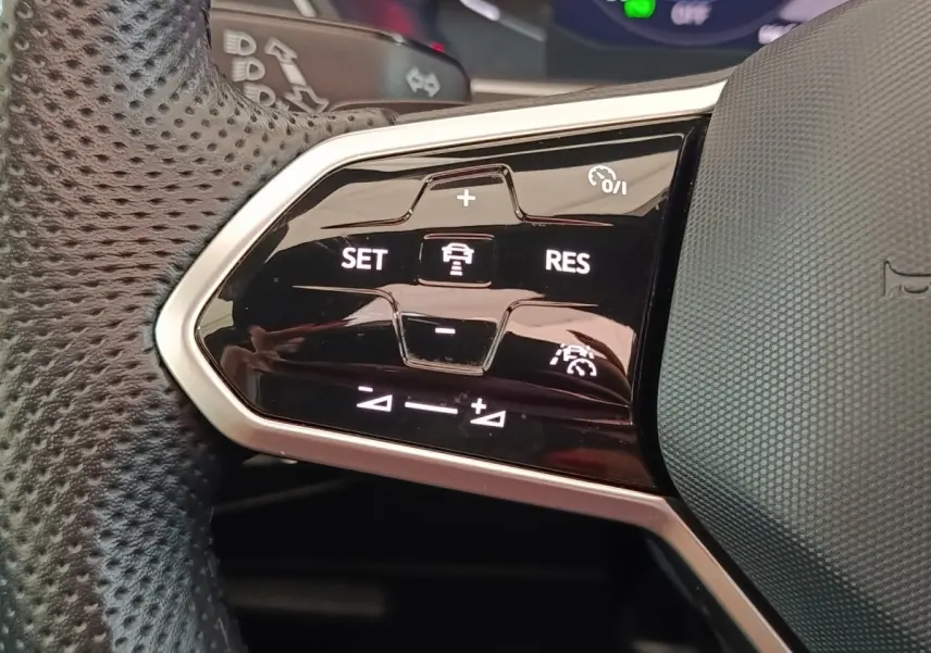 Gros plan sur les commandes du volant cuir perforé du Volkswagen Tiguan 1.4 eHybrid blanc, boutons de régulateur adaptatif.