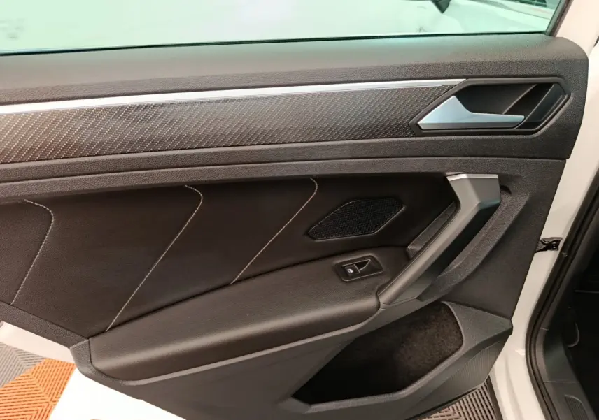 Vue rapprochée de la porte avant gauche noire avec surpiqûres et insert décoratif du Volkswagen Tiguan blanc 2023.