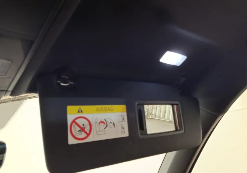 Pare-soleil intérieur noir avec miroir et avertissement airbag, vue en léger contre-plongée depuis l'habitacle.
