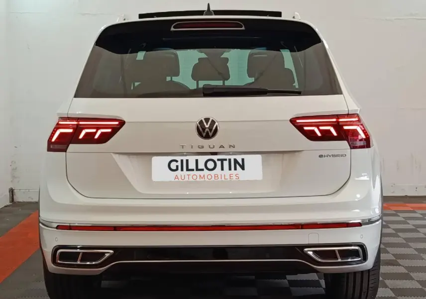 Vue arrière d'un Volkswagen Tiguan blanc hybride rechargeable avec feux LED allumés et double sortie d'échappement intégrée.