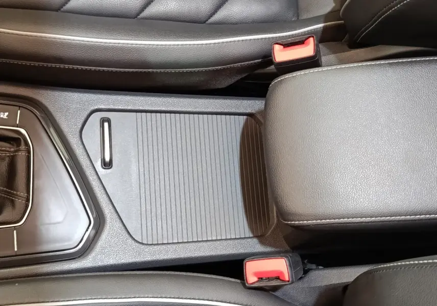Vue rapprochée de la console centrale noire avec accoudoir et ceintures de sécurité rouges du Volkswagen Tiguan blanc 2023.