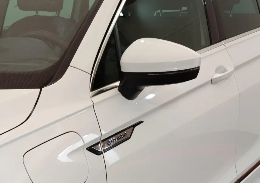 Gros plan sur la porte avant gauche blanche d’un Volkswagen Tiguan eHybrid avec rétroviseur et badge eHybrid visible.