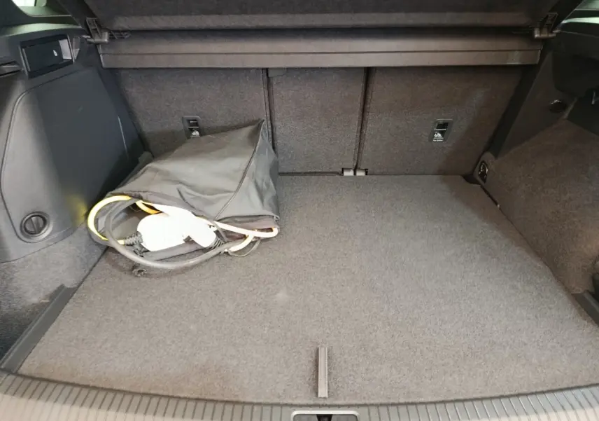 Vue du coffre arrière du Volkswagen Tiguan blanc 1.4 eHybrid 2023, avec câble de recharge et tapis gris.
