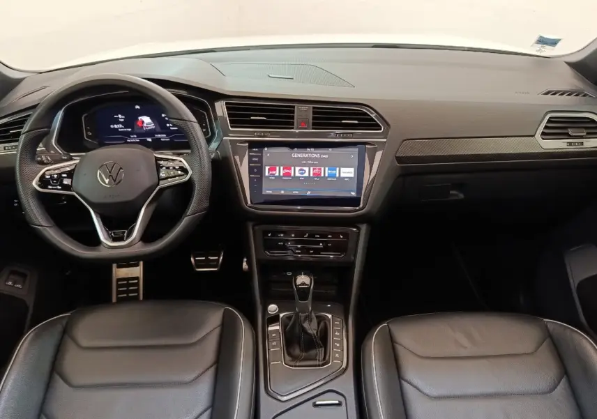 Vue intérieure avant du Volkswagen Tiguan blanc 2023, tableau de bord moderne avec écran tactile central et volant cuir multifonctions.