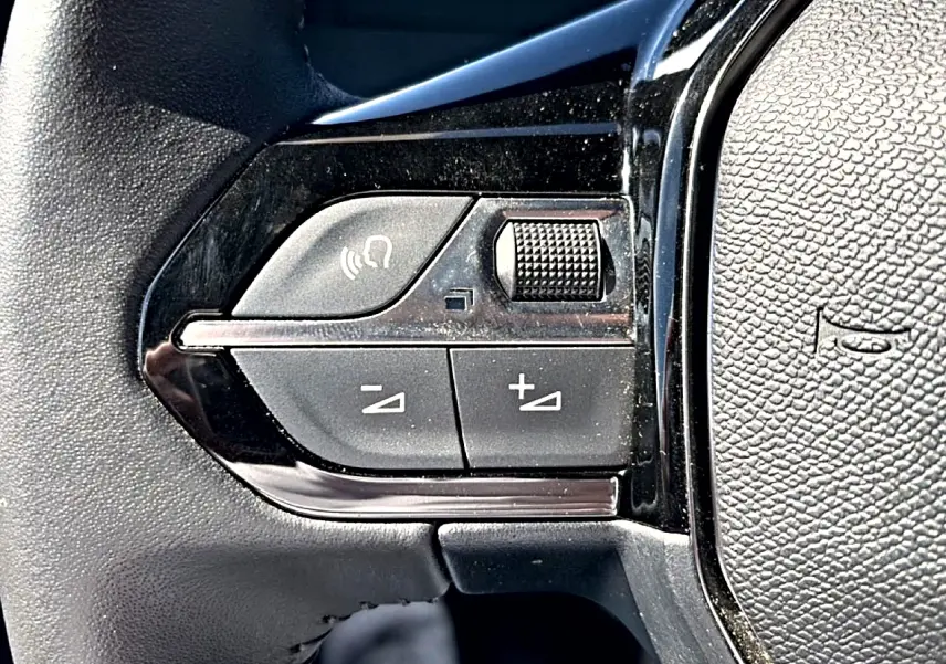 Gros plan sur les commandes de volume et de fonction vocale sur le volant noir du Peugeot 2008 gris.