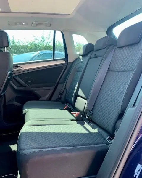 Vue intérieure arrière droite du Volkswagen Tiguan bleu, sièges arrière en tissu matelassé et toit ouvrant panoramique visible.