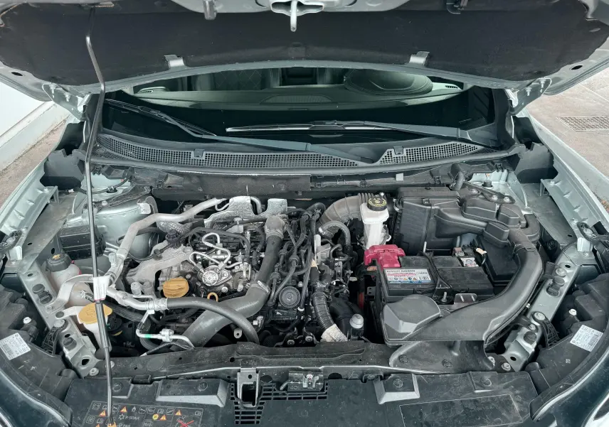 Moteur essence du Renault Kadjar gris vu de dessus avec capot ouvert, montrant les composants mécaniques et la batterie.