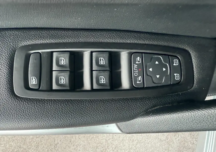 Gros plan sur les commandes de lève-vitres et réglages des rétroviseurs côté conducteur d'un Renault Kadjar gris.