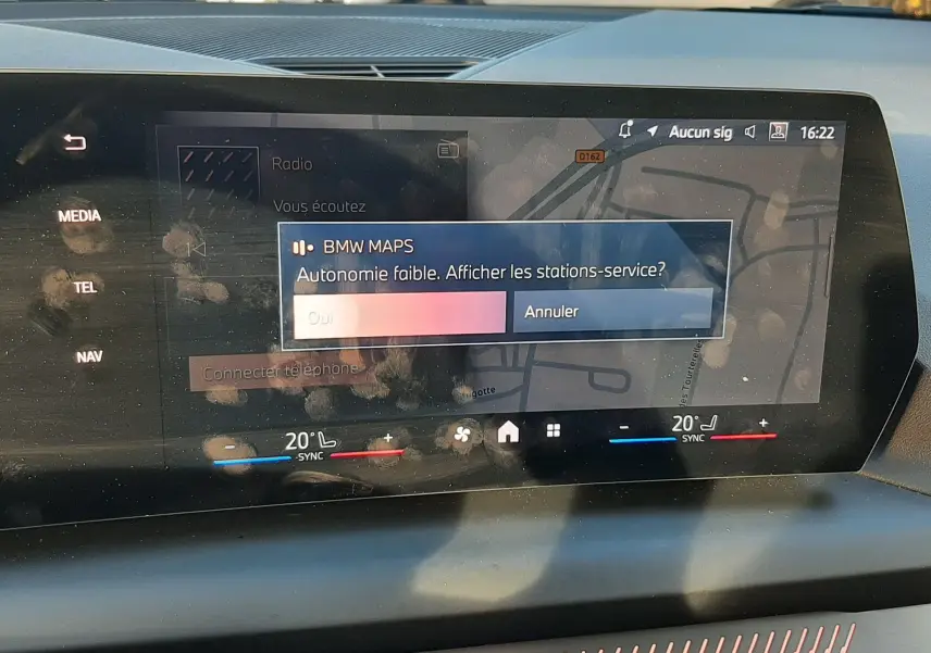 Écran tactile central de la BMW Série 1 F70 120D 2025 affichant une alerte d'autonomie faible avec interface de navigation.